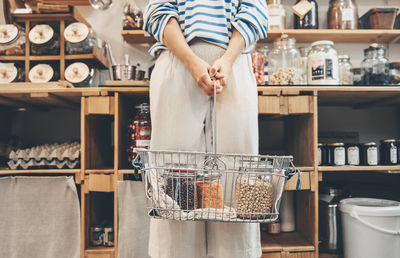 Customer holding jars filled with lentils in shopping basket at shop