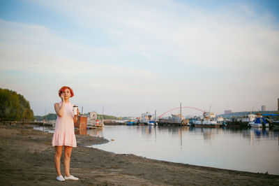 Full length of woman holding disposable cup while using phone at beach