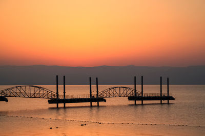 Silhouette bridge over sea against orange sky