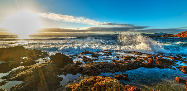 Waves splashing on rocks at shore against blue sky