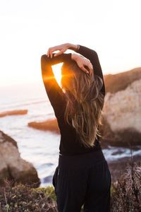 Rear view of woman standing at beach during sunset