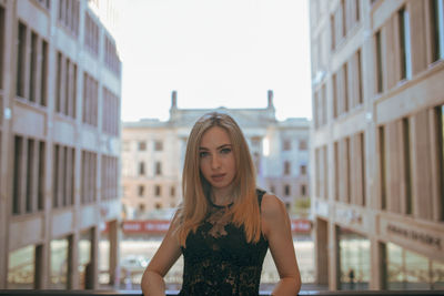 Portrait of beautiful young woman standing against buildings in city