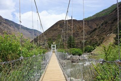 Footbridge over mountain against sky