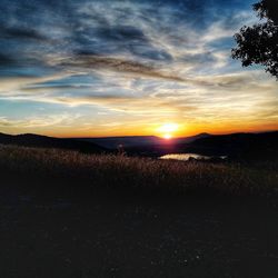 Scenic view of silhouette field against sky at sunset