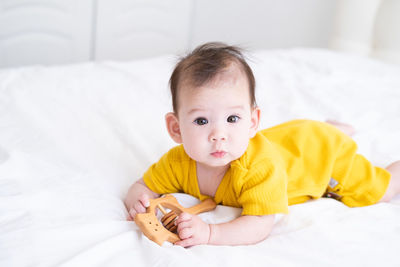 Healthy asian baby girl in yellow bodysuit playing with wooden toys on white bedding