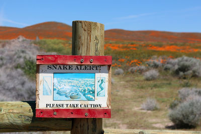 Close-up of information sign on wooden post against sky