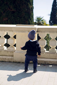 Boy in the hat and pants standing on the street next to the fence in the arboretum back