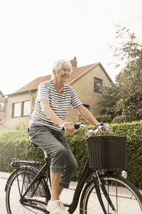 Smiling senior woman cycling on road by house