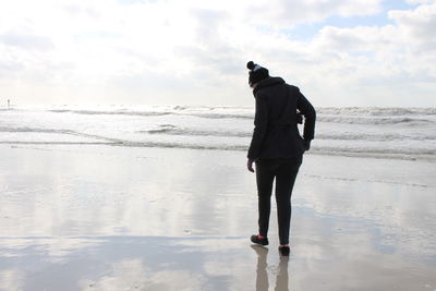 Rear view of woman standing on beach against sky