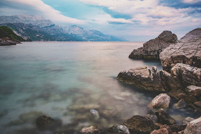 Rocks in river by mountains against sky