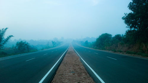 Empty road along trees and against sky