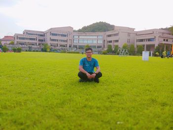 Portrait of man sitting on field against buildings