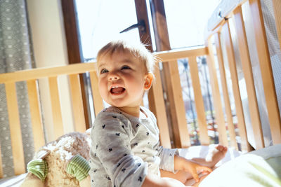 Cute girl looking away while sitting on infant bed