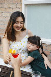 Smiling mother holding juice sitting with girl outdoors