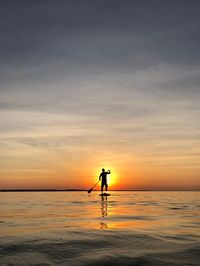 Silhouette of man paddleboarding on sea against sky during sunset