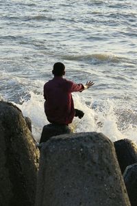 Rear view of man sitting on steps at sea shore