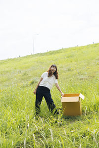 Full length of woman holding box while standing on grass against sky