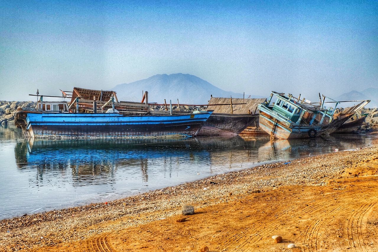 water, nautical vessel, moored, boat, beach, mode of transport, transportation, sea, blue, sky, shore, tranquility, tranquil scene, sand, clear sky, nature, scenics, mountain, beauty in nature, built structure