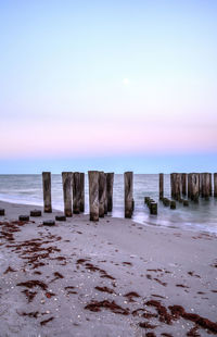 Wooden posts on beach against sky during sunset