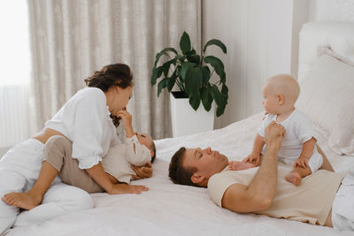 Family with two kids on the bed having fun. mather, father baby and toddler sons are happy in the