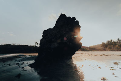 Rock formation on beach against sky during sunset