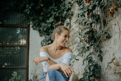 Smiling young woman sitting by wall