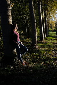 Full length of girl leaning on tree trunk in forest