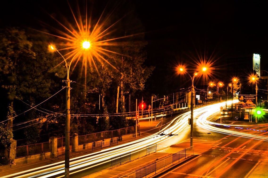 LIGHT TRAILS ON ROAD IN CITY AT NIGHT