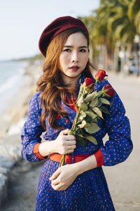 Close-up portrait of beautiful woman holding rose standing at beach