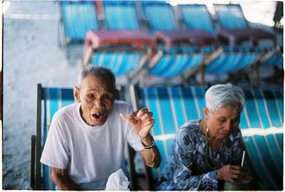 Senior people sitting on deck chair while having food at beach