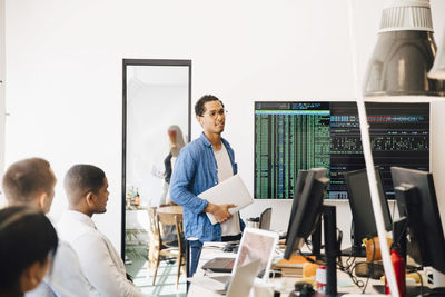 Computer hacker explaining code on television screen to programmers during meeting in creative office