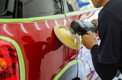 Midsection of man working with equipment on car