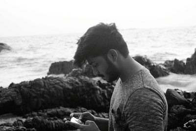 Side view of young man sitting on rock against sea