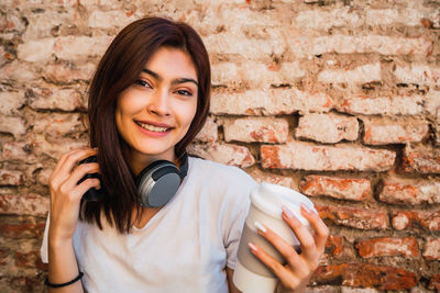 Portrait of smiling young woman standing against brick wall