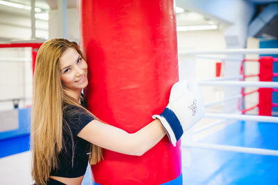 Portrait of young woman holding punching bag while standing in ring