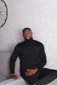 Portrait of young man sitting on sofa against wall