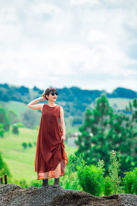 Young woman wearing sunglasses standing on mountain against cloudy sky