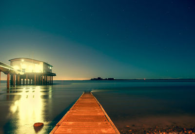 Pier over sea against clear sky at night