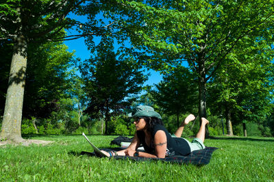 Woman reading paper while lying down on field against trees