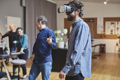 Businessman using virtual reality simulator while standing by colleagues in creative office