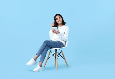 Portrait of young woman sitting on chair against blue background