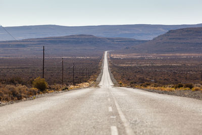 Country road leading towards mountains against sky