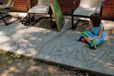 Full length of girl drawing through chalk on sidewalk
