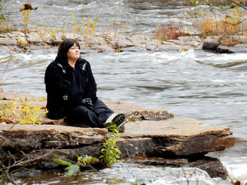 Young woman sitting on rock by river