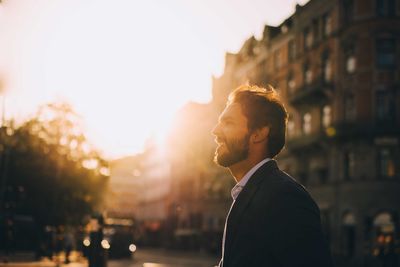 Side view of smiling man standing against sky in city