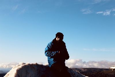 Portrait of man wearing warm clothing while standing against blue sky