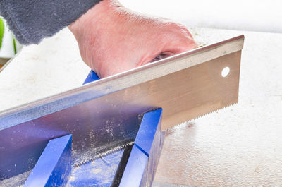 Cropped image of man cutting metal with saw in workshop