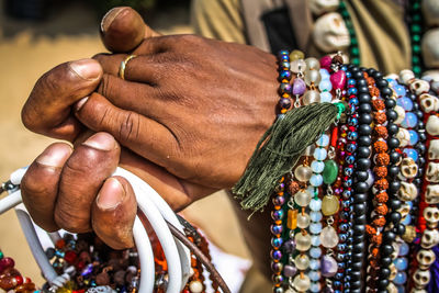Cropped hand of man selling bead necklaces at beach