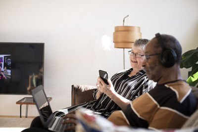 Woman using smart phone sitting by man with laptop at home