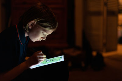 Profile of tween drawing with stylus on tablet indoors low lit